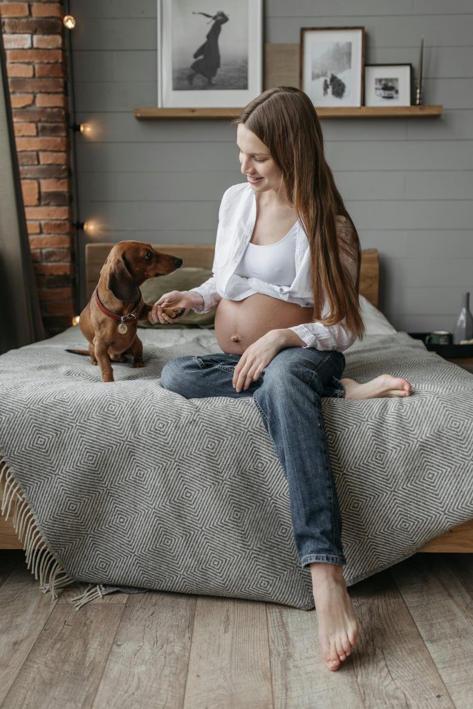 A pregnant woman shares a tender moment with her dachshund while sitting comfortably on a bed.